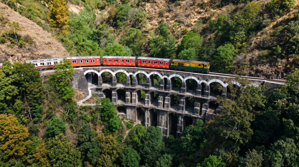 Aerial view of a heritage toy train crossing a stone viaduct in the Himalayas